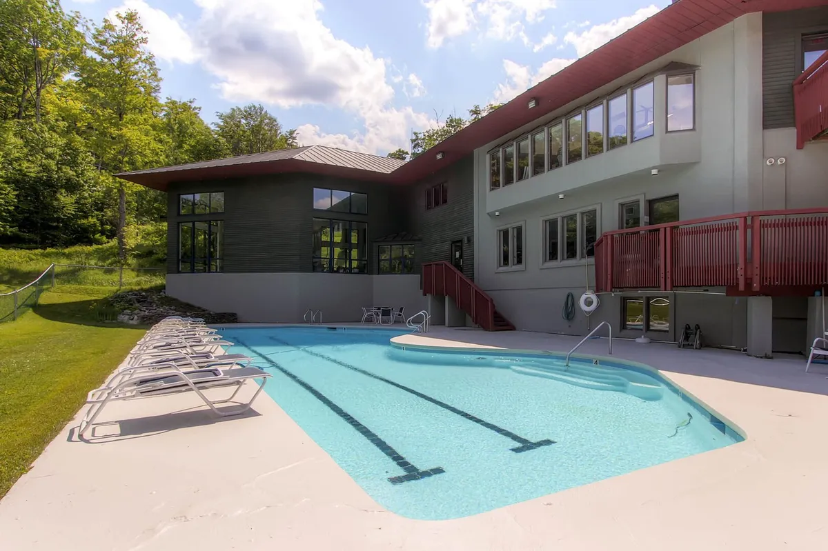 An outdoor pool surrounded by a sunny deck, modern architecture, and lush greenery, inviting guests to swim, sunbathe, or gather outdoors during the warmer months.