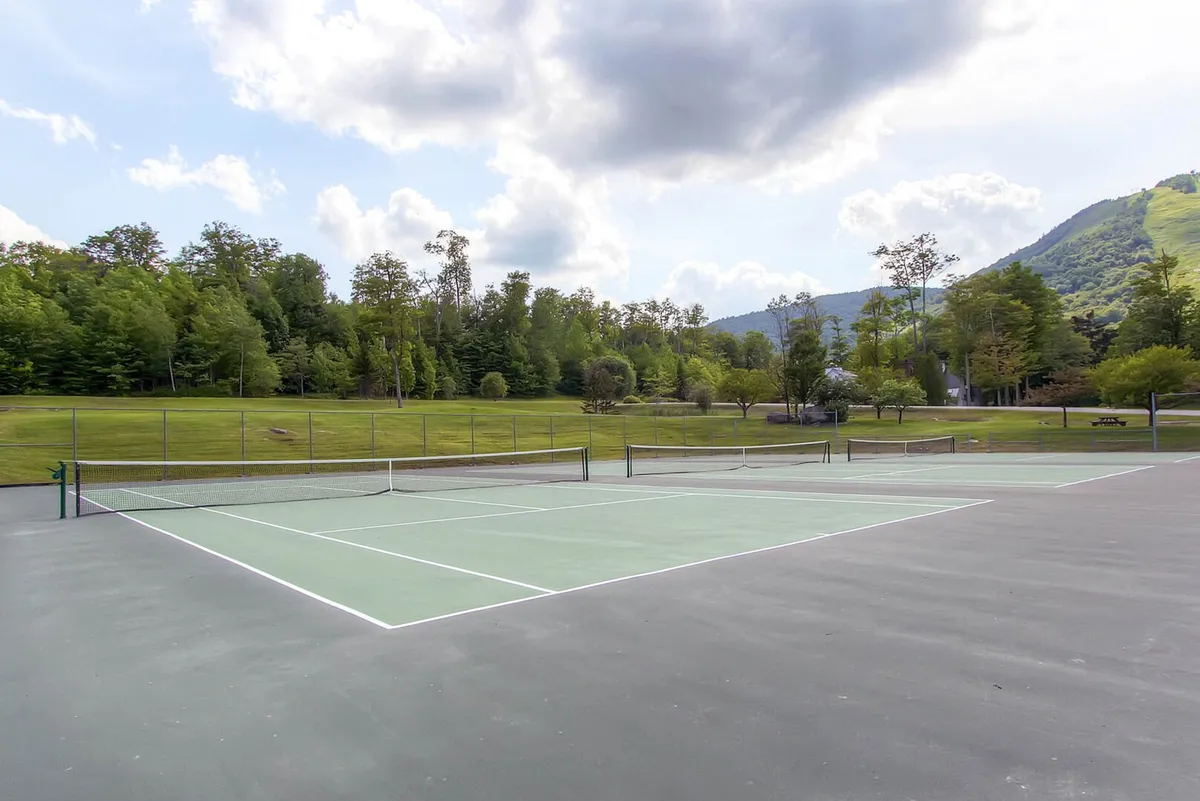 An exterior scene featuring tennis courts surrounded by greenery and mountains in the backdrop, inviting guests to enjoy outdoor activities beyond skiing.