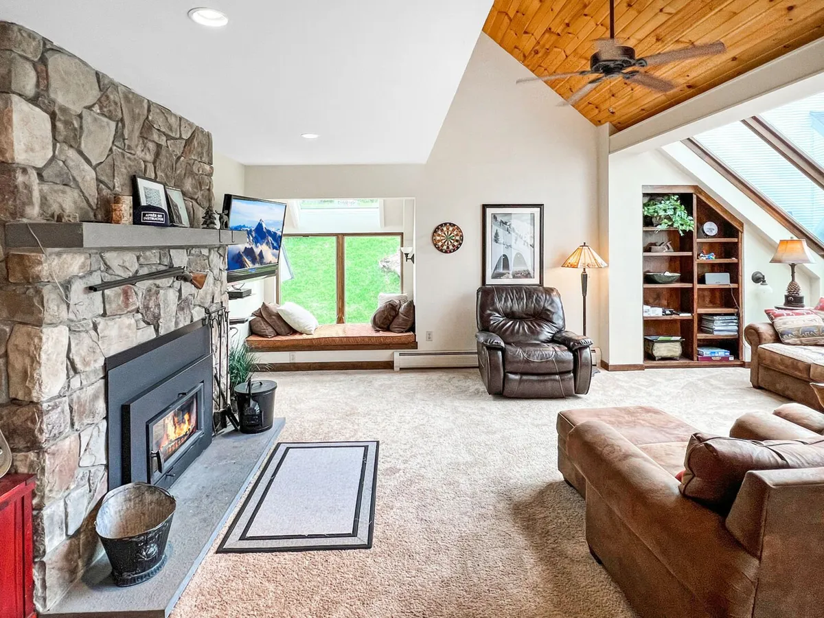 A cozy living area with a striking stone fireplace, large windows bringing in natural light, comfortable seating, and a wooden ceiling. The scene exudes warmth and comfort—an ideal retreat after time spent outdoors in any season.