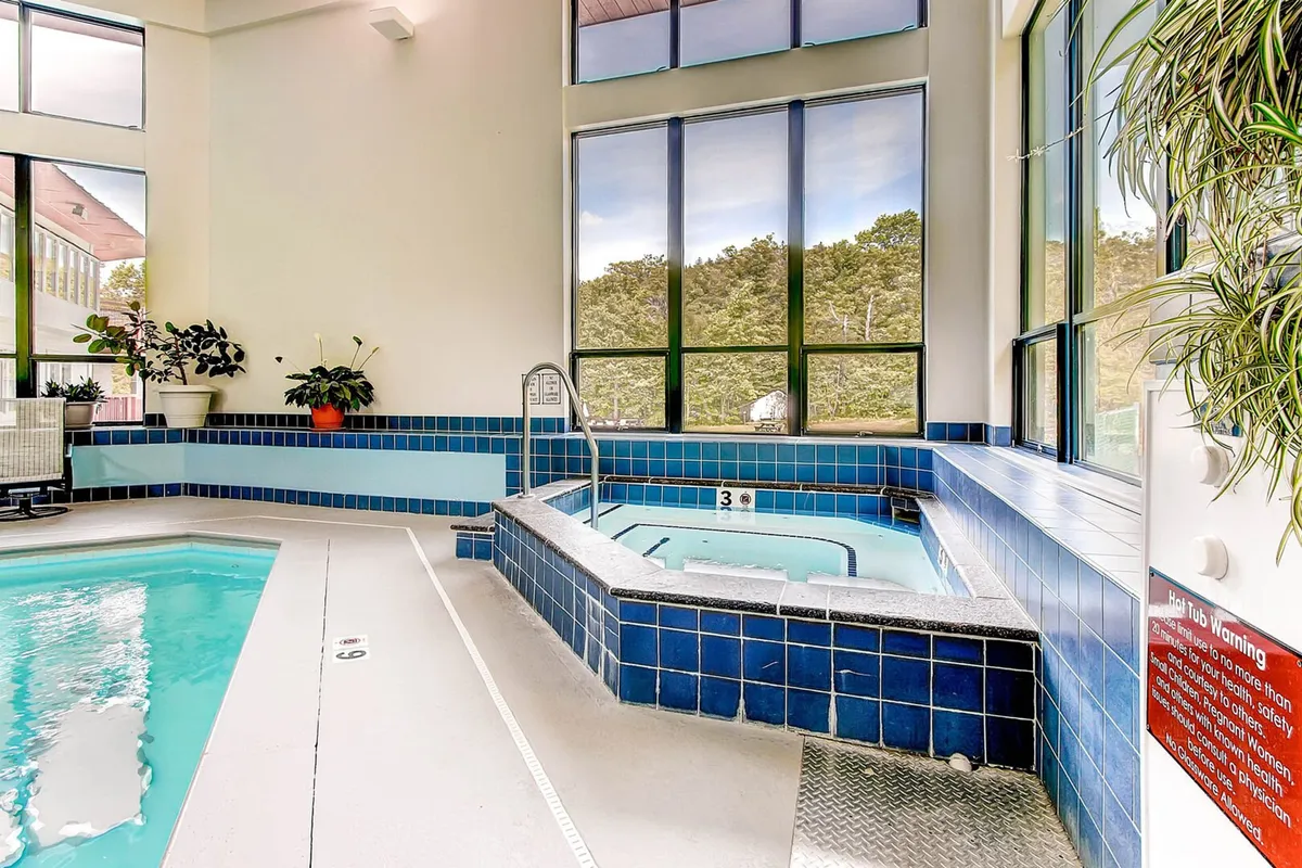An inviting indoor pool and hot tub area with large windows letting in natural light, surrounded by lush indoor plants. The tranquil atmosphere is designed for swimming, soaking, and socializing year-round, offering a true resort experience.