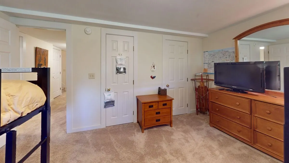 A den/TV room is arranged with a bunk bed, a television, a dresser, and a wooden nightstand, creating a functional hangout spot for watching movies or enjoying downtime. The décor is casual and relaxed, perfect for teens or extra guests looking for their own space.