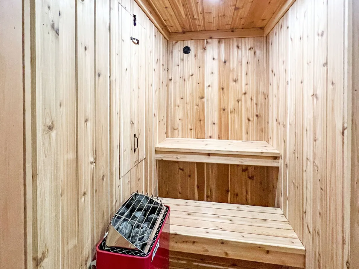 The tranquil sauna features wooden benches, a classic stone heater, and warm wood-paneled walls, evoking a spa-like ambiance. This is an ideal spot for relaxation and rejuvenation after an active day.